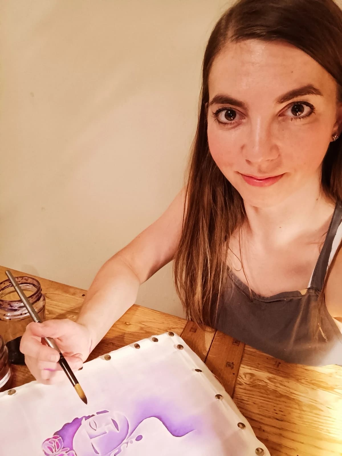 Ania smiling at her table, painting violet dye onto silk stretched on a frame