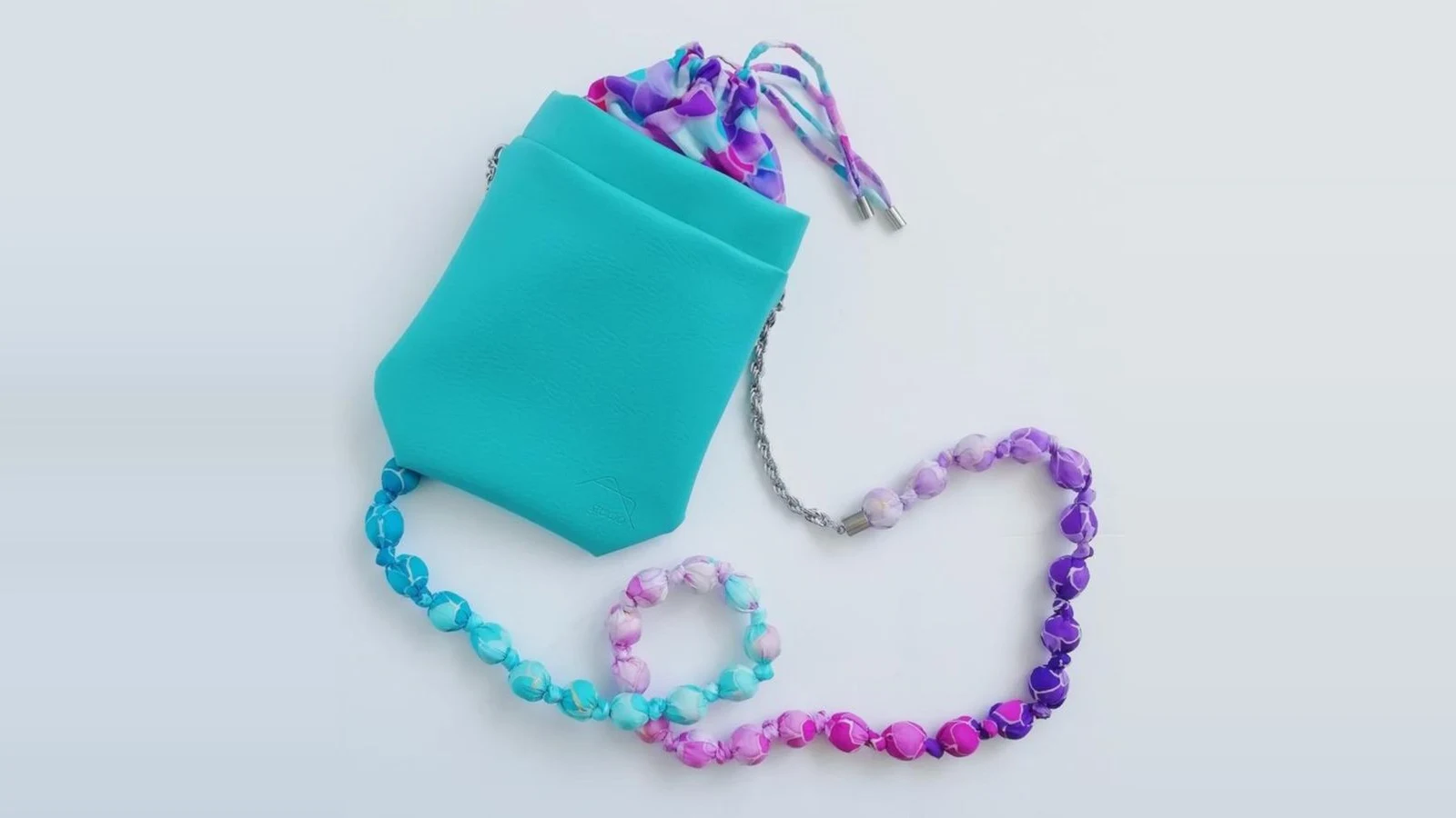 A handmade silk bead necklace and bracelet in turquoise, pink and purple, beside a matching turquoise pouch on a pale background.