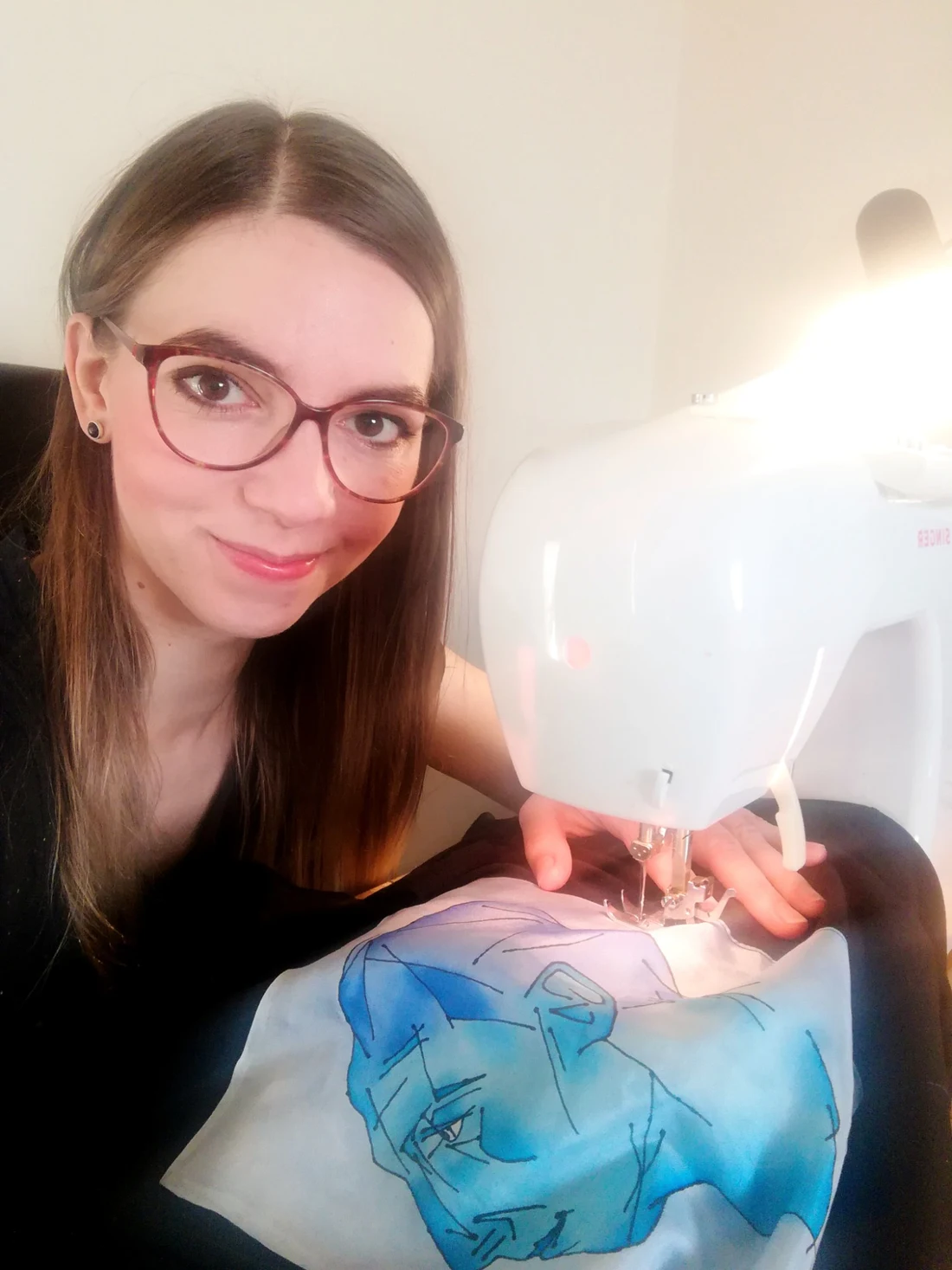 Ania at her white sewing machine, stitching the edge of a blue hand painted silk piece.