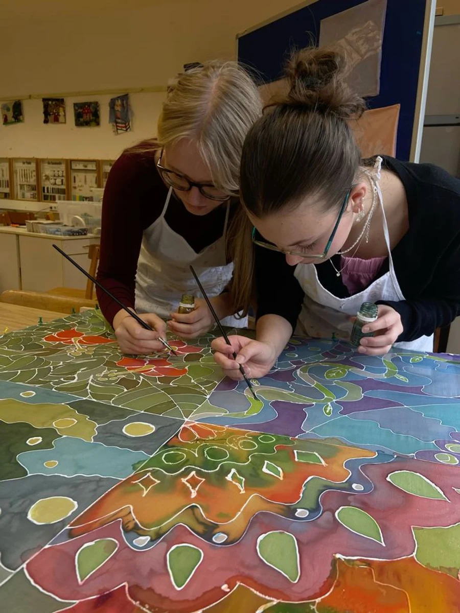Two people painting a large colourful silk piece together.