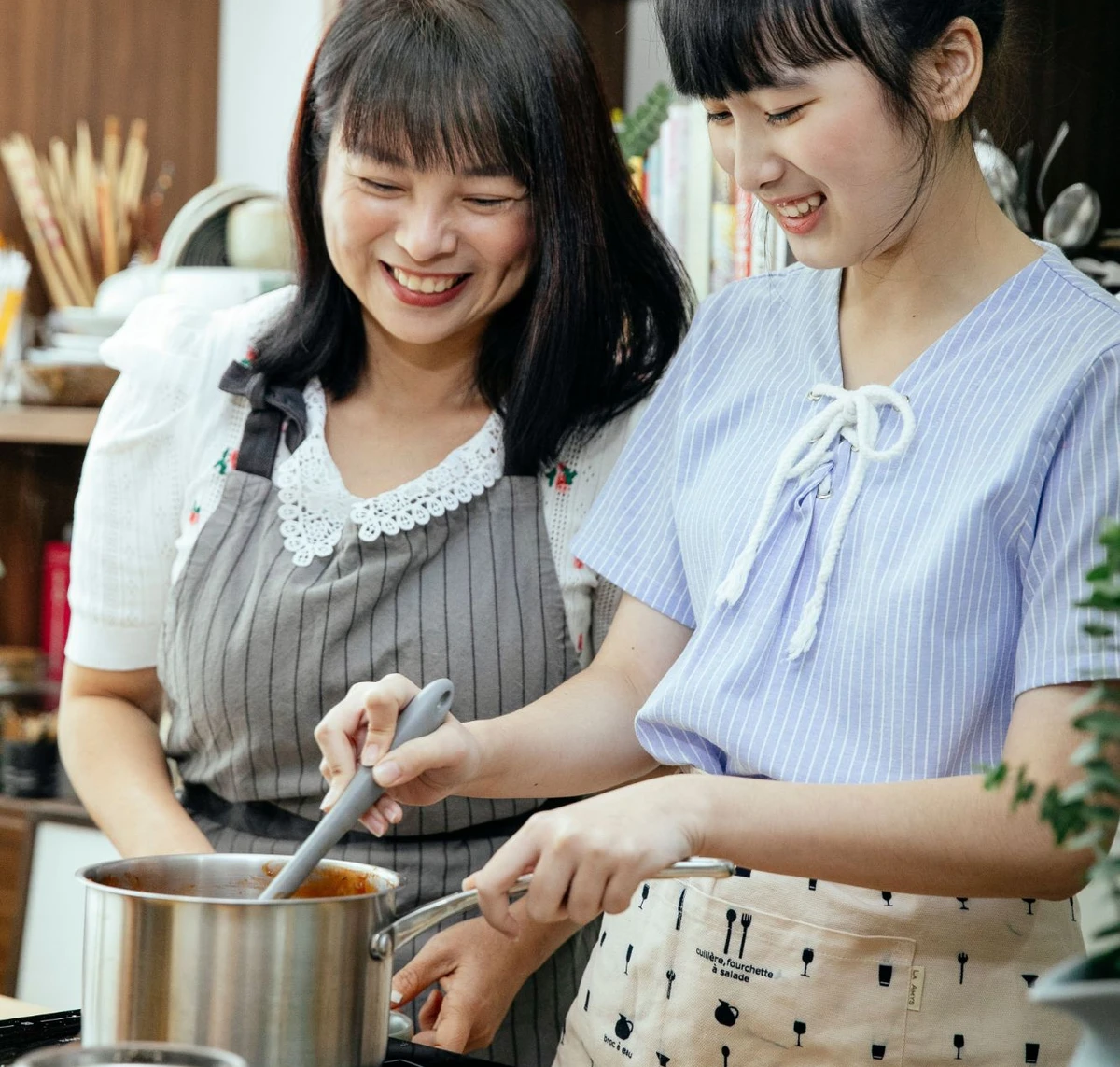 Mother and adult daughter preparing food together in a home kitchen.