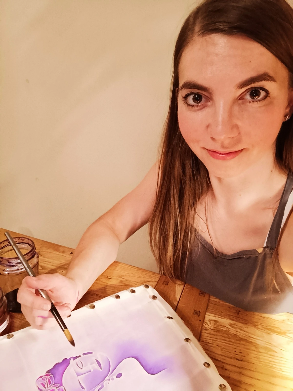 Ania at a wooden table, laying violet dye onto stretched white silk with a fine brush.