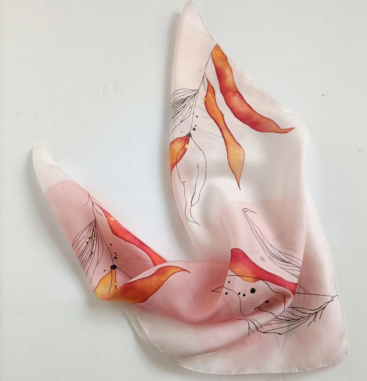 A finished hand-painted silk scarf in soft pink, with coral and orange petals and fine ink lines.