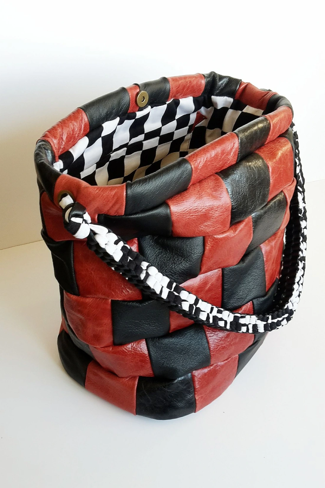 A handmade bag woven from strips of red and black leather, with a plaited strap.