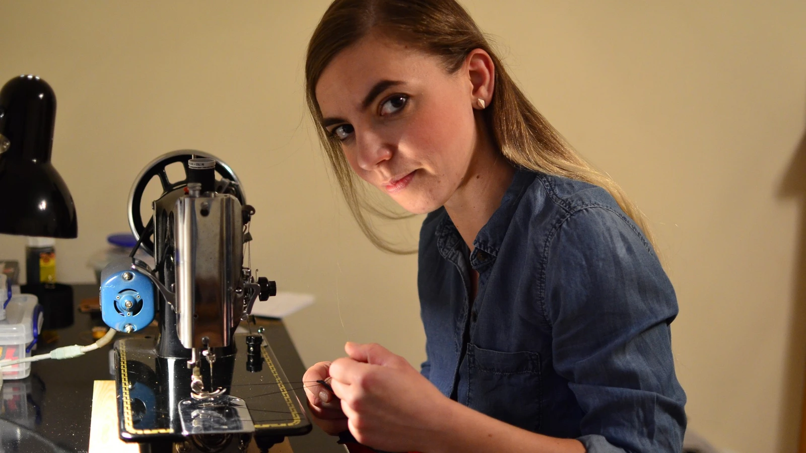 Ania at her vintage sewing machine, looking up from her work with the thread in her hands.