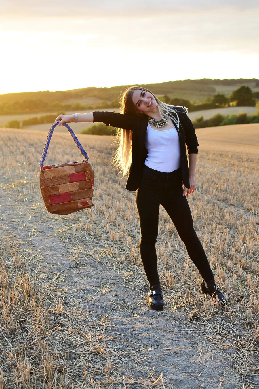 Ania standing in a field at sunset, holding a leather bag she made herself.