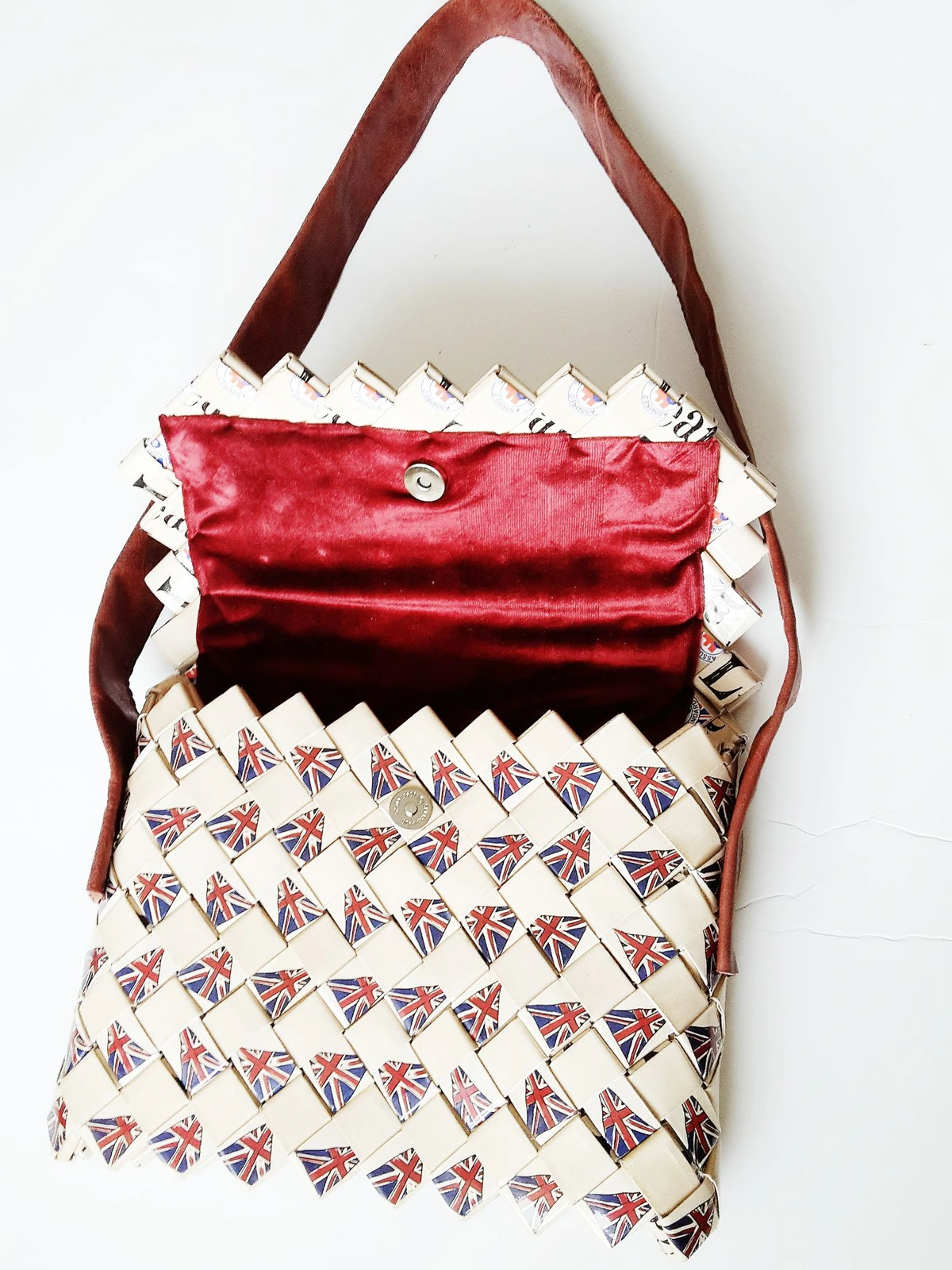 A handbag woven by hand from folded paper printed with Union Jack flags, with a deep red flap and a leather strap.