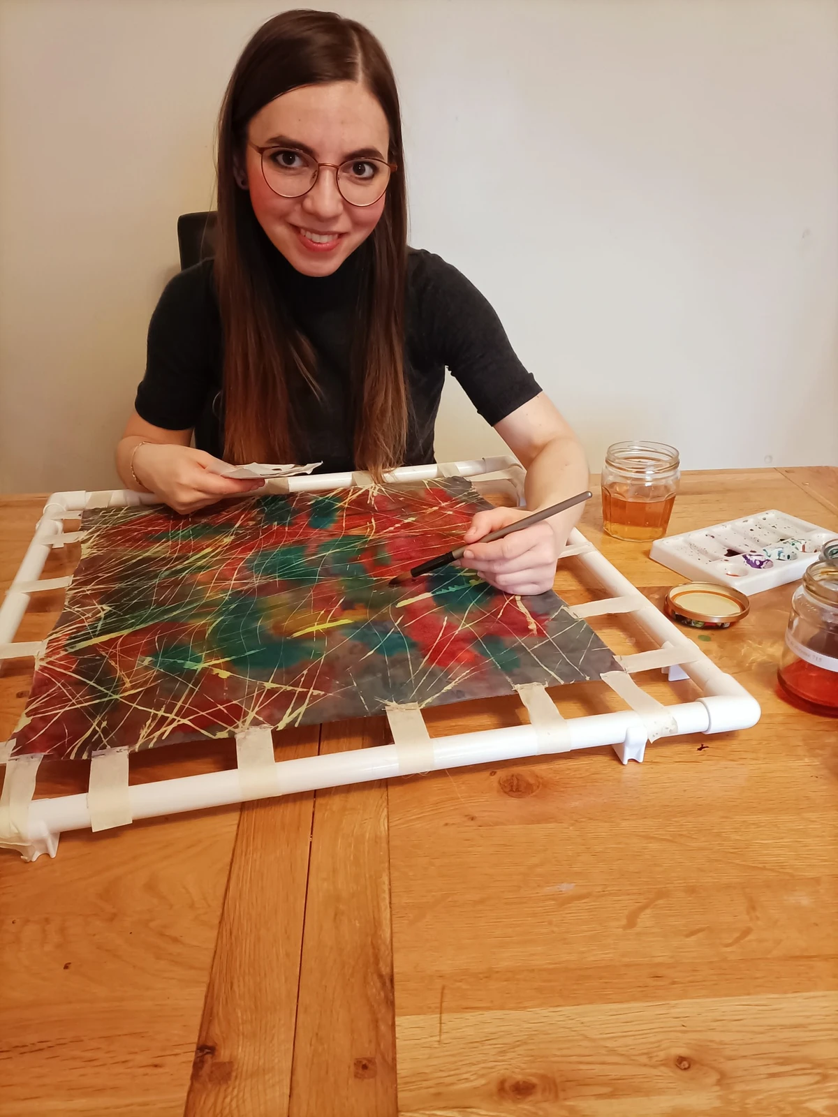 Ania painting colourful silk stretched on a frame.