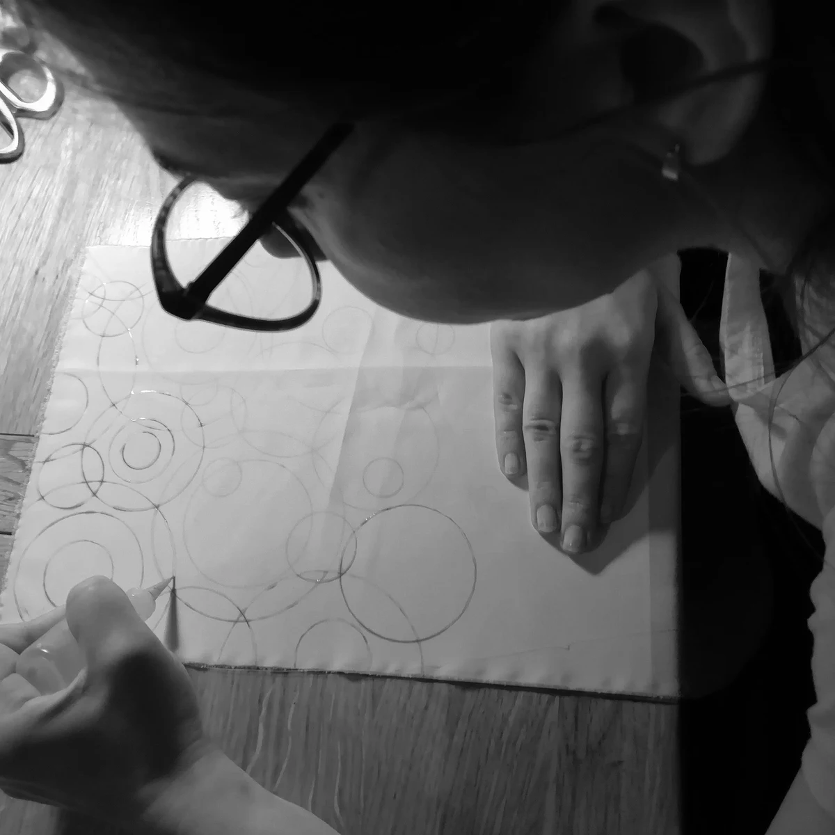 Ania leaning close over a piece of stretched silk, drawing overlapping circles onto it.