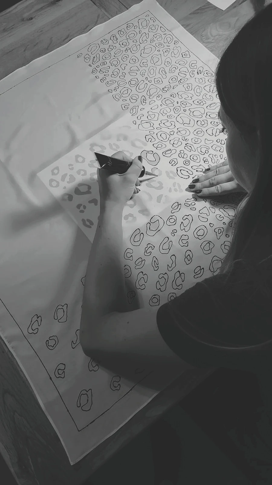 Ania seen from behind, drawing the outline of a leopard pattern onto white silk with a fine applicator.