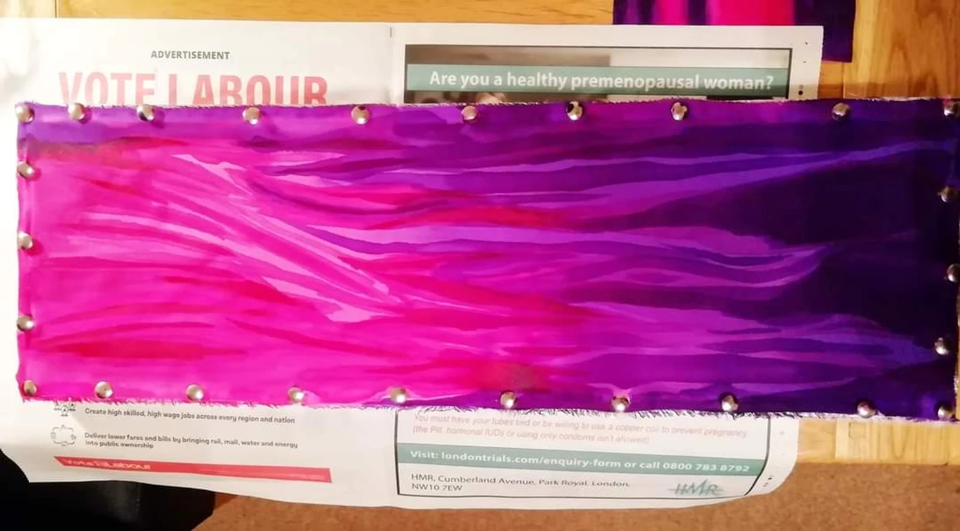 A long piece of silk hand-painted in pink and purple, pinned out flat along every edge.